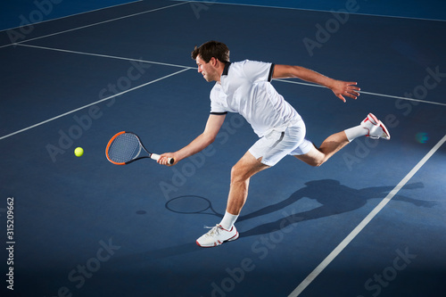 Male tennis player playing tennis, reaching tennis racket on tennis court