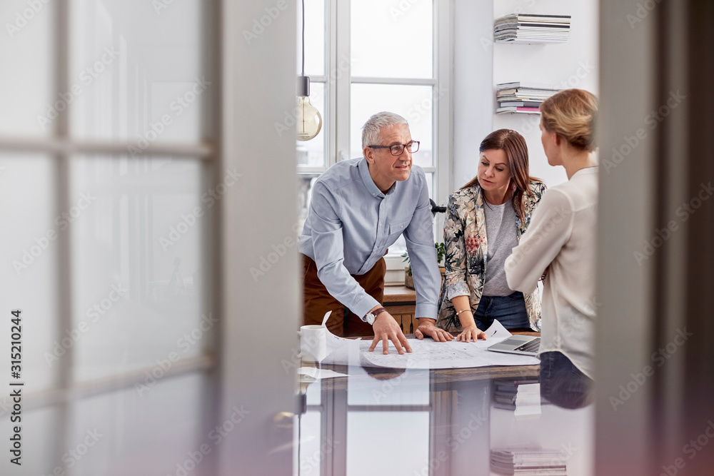 © Agnieszka Olek/Caia Image - Architects reviewing, discussing blueprints in conference room meeting