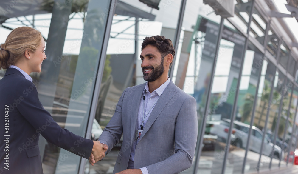 Car salesman greeting, shaking hands female customer outside car dealership showroom Car salesman greeting, shaking hands female customer outside car dealership showroom
