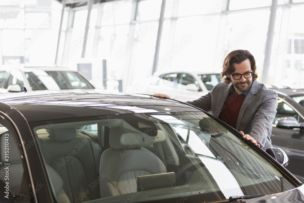 Male customer eyeing new car in car dealership showroom Male customer eyeing new car in car dealership showroom