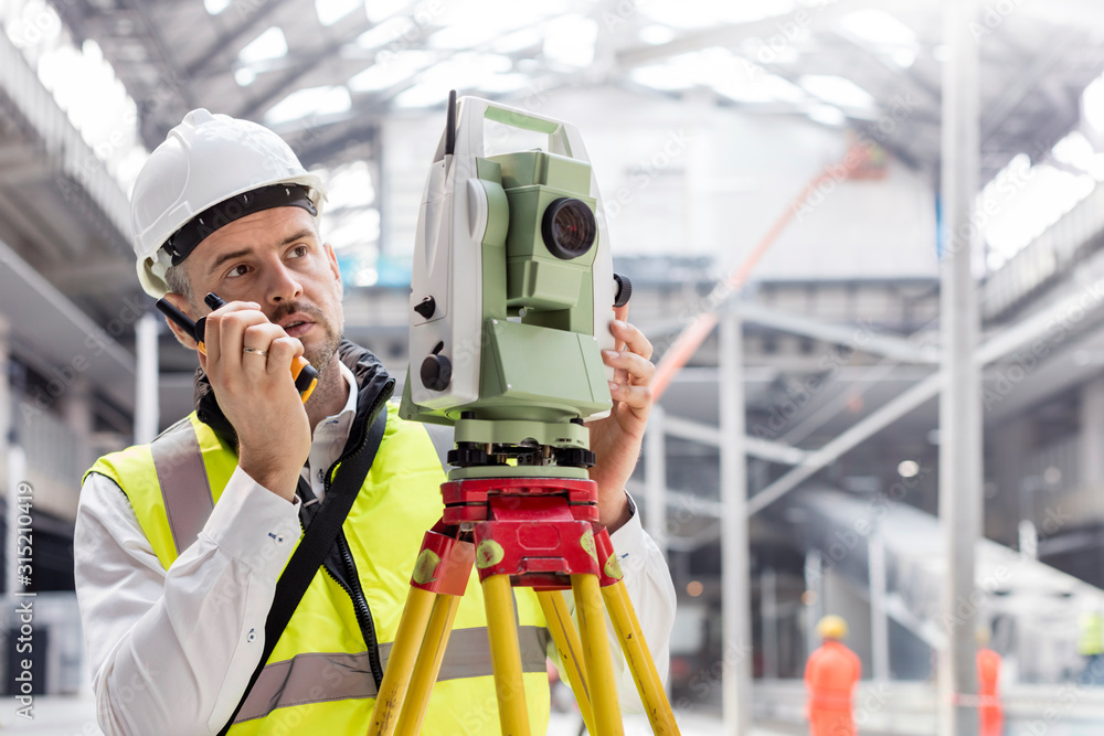Male engineer using walkie-talkie and theodolite at construction site Male engineer using walkie-talkie and theodolite at construction site