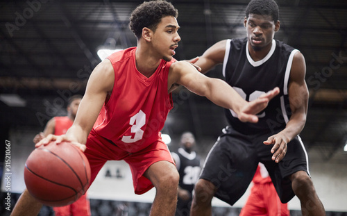 Young male basketball player dribbling the ball, protecting from defender in basketball game