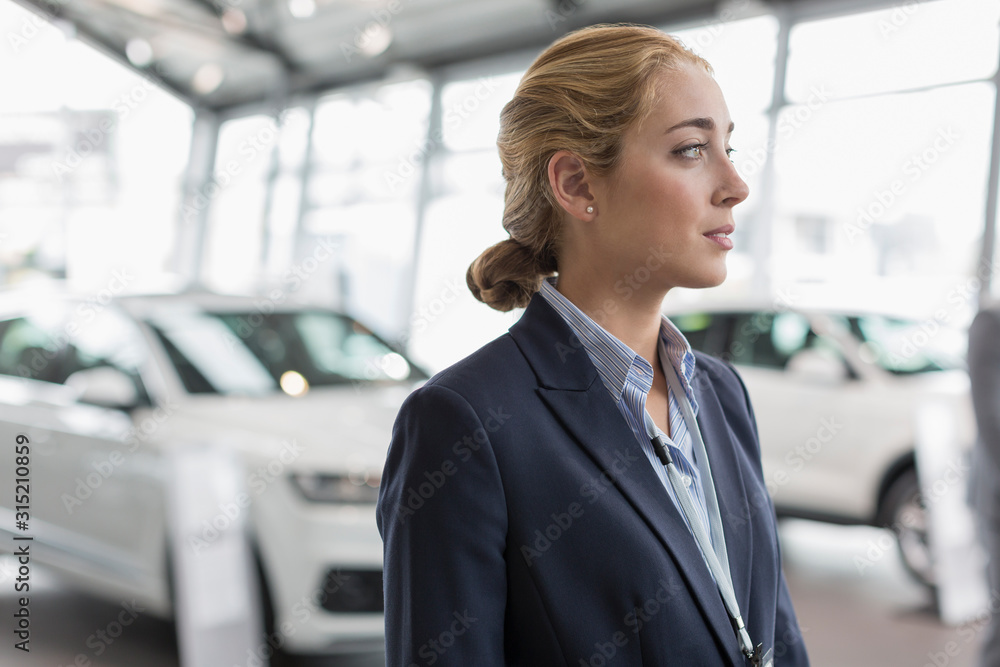 Pensive car saleswoman looking away in car dealership showroom Pensive car saleswoman looking away in car dealership showroom