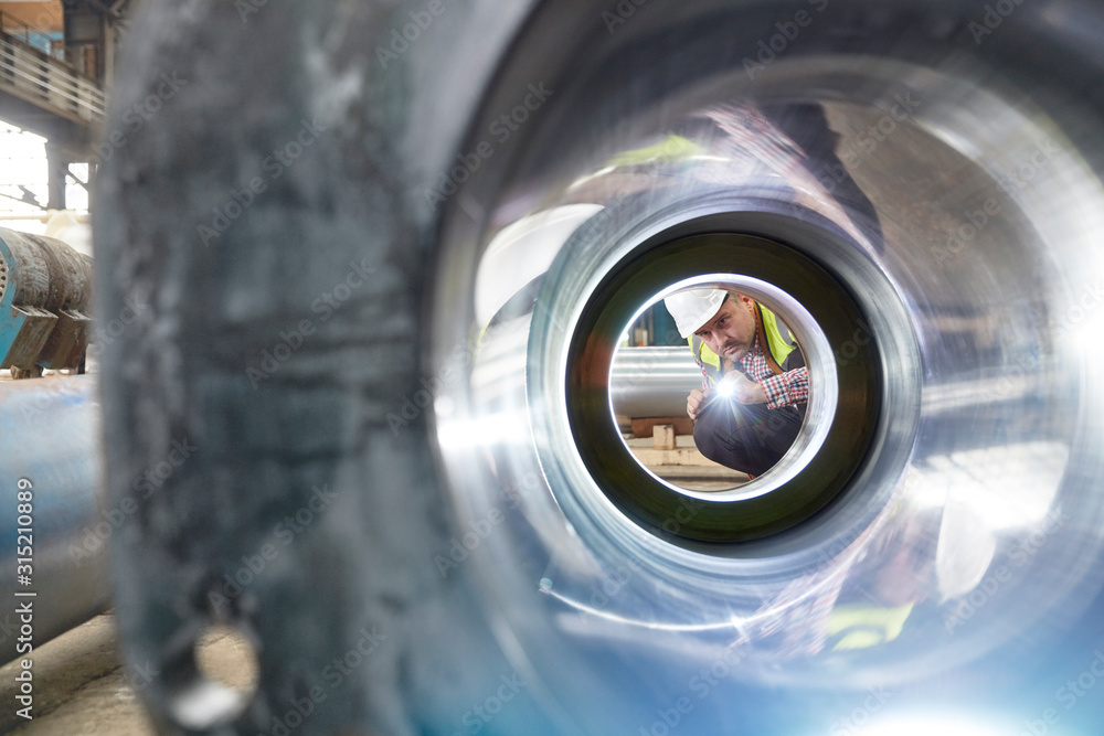 Male engineer with flashlight examining steel pipe in factory Male engineer with flashlight examining steel pipe in factory