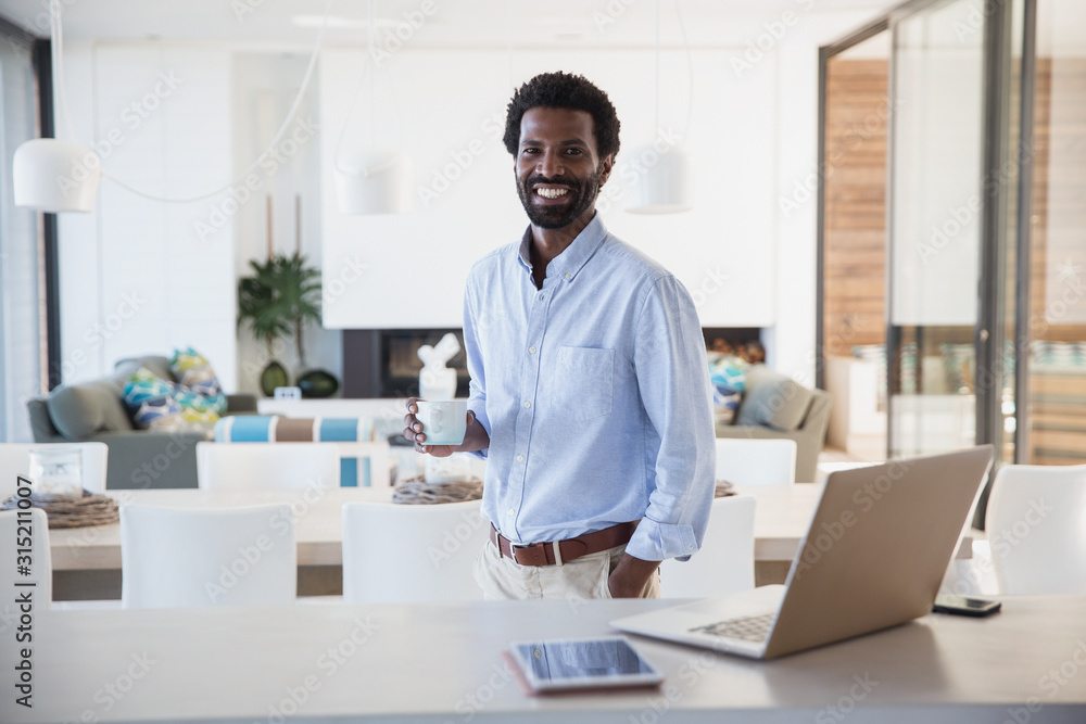Portrait smiling businessman drinking coffee at laptop in kitchen Portrait smiling businessman drinking coffee at laptop in kitchen