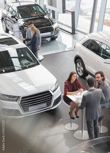 Car sales people meeting at table in car dealership showroom