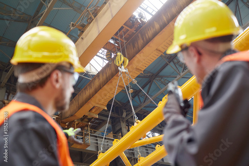 Male worker using walkie-talkie to guide hydraulic crane lowering equipment in factory photo