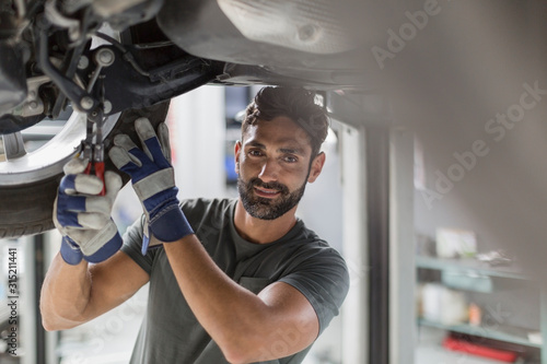 Portrait confident male auto mechanic working under car in auto repair shop photo