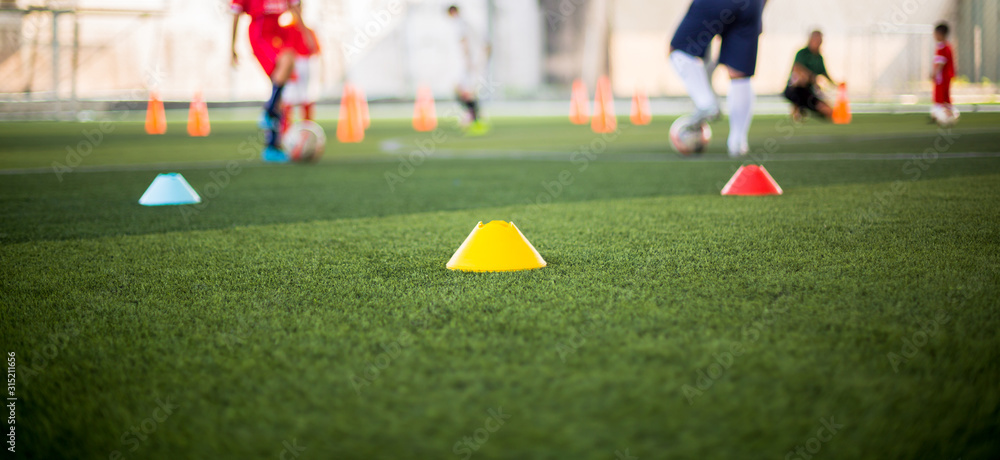 Marker Cone on green artificial turf with blurry kid soccer players are training background. Soccer academy. Marker Cone on green artificial turf with blurry kid soccer players are training background. Soccer academy.