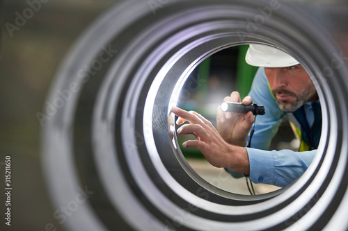 Male engineer with flashlight inspecting steel cylinder