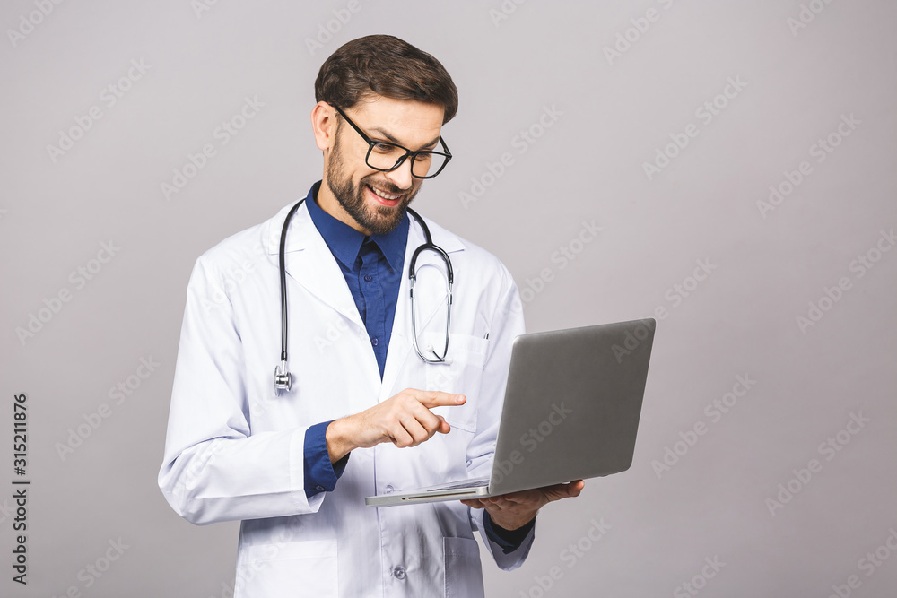Concentrated male doctor using laptop isolated over grey background. Concentrated male doctor using laptop isolated over grey background.