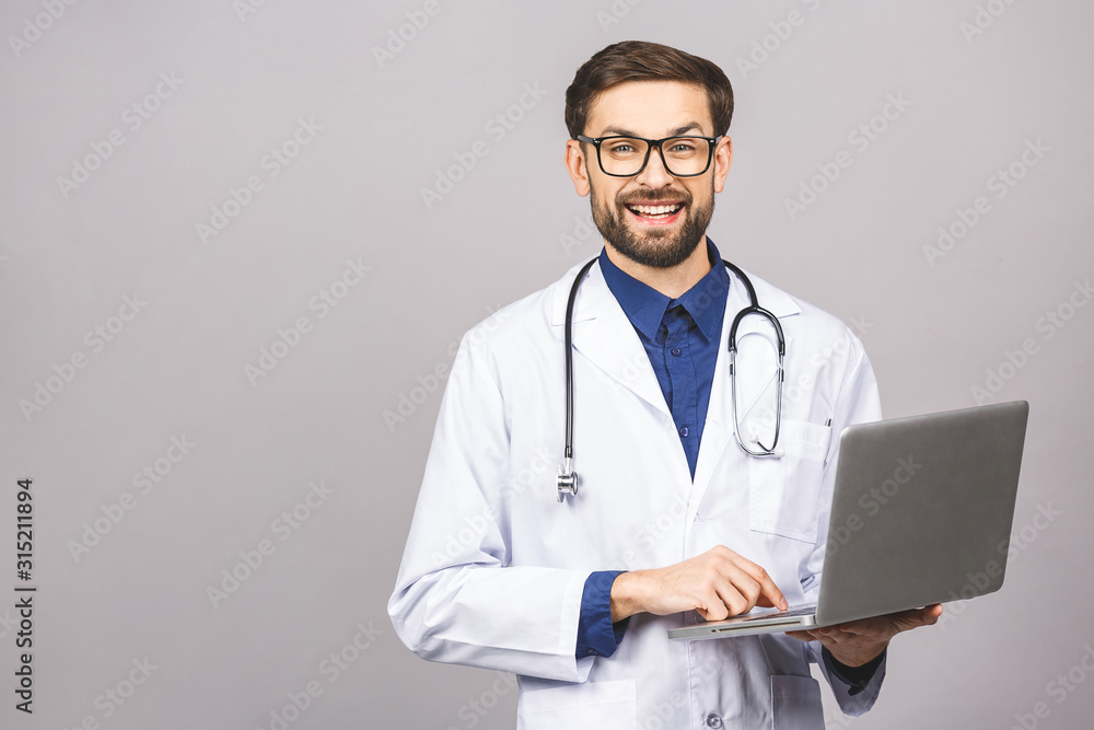 Concentrated male doctor using laptop isolated over grey background. Concentrated male doctor using laptop isolated over grey background.