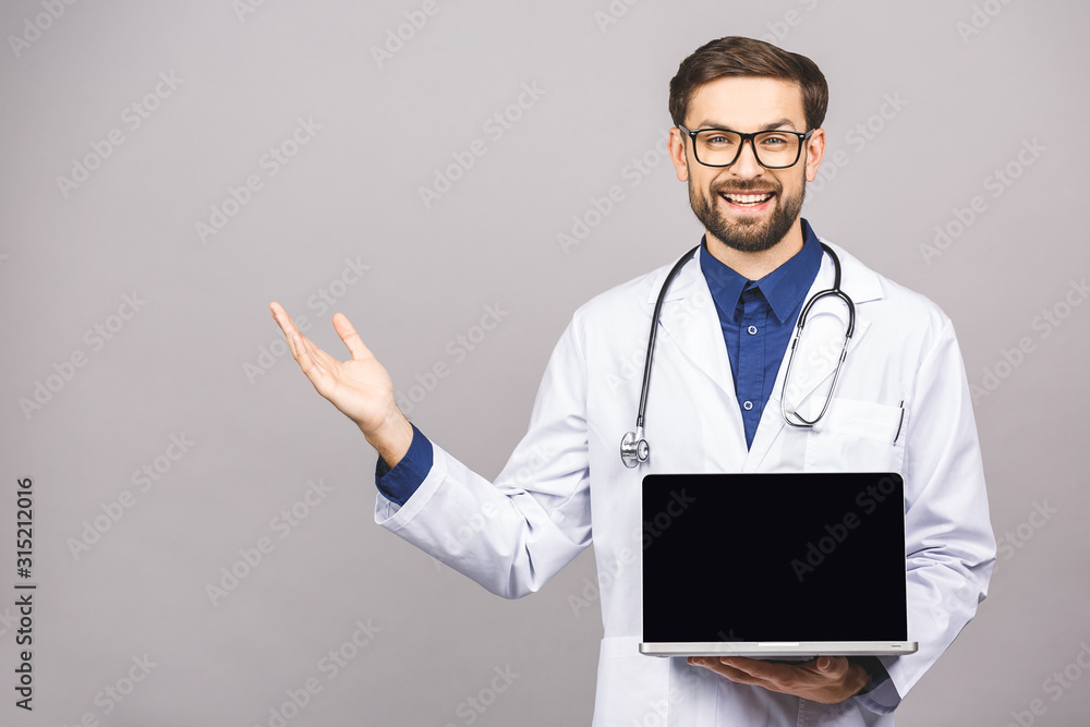 Concentrated male doctor using laptop isolated over grey background. Concentrated male doctor using laptop isolated over grey background.
