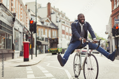 Playful young businessman commuting, riding bicycle on urban street photo