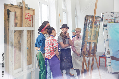 Art students instructor examining, critiquing painting in art class studio