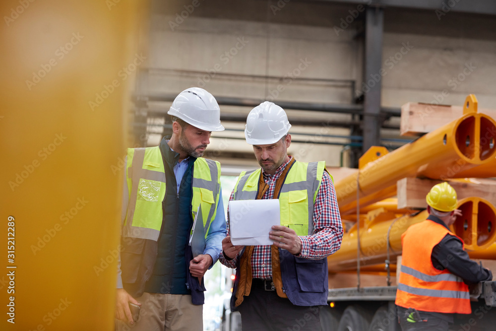 Male foreman and worker reviewing paperwork in factory Male foreman and worker reviewing paperwork in factory