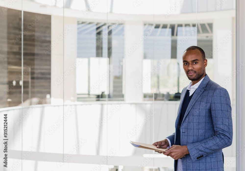 Portrait confident businessman with paperwork in office atrium Portrait confident businessman with paperwork in office atrium