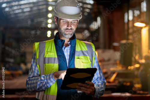Male engineer working at glowing digital tablet in dark factory photo