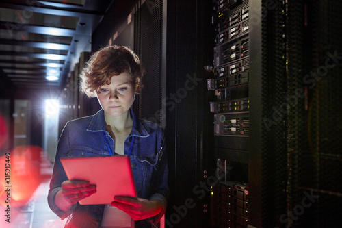 Focused female IT technician using digital tablet in server room photo