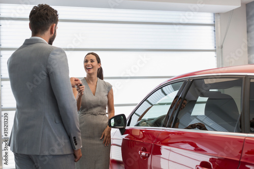 Car salesman giving keys to new car to female customer in car dealership