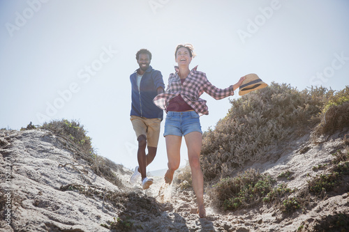 Playful, energetic multi-ethnic couple running on sunny summer sbeach path