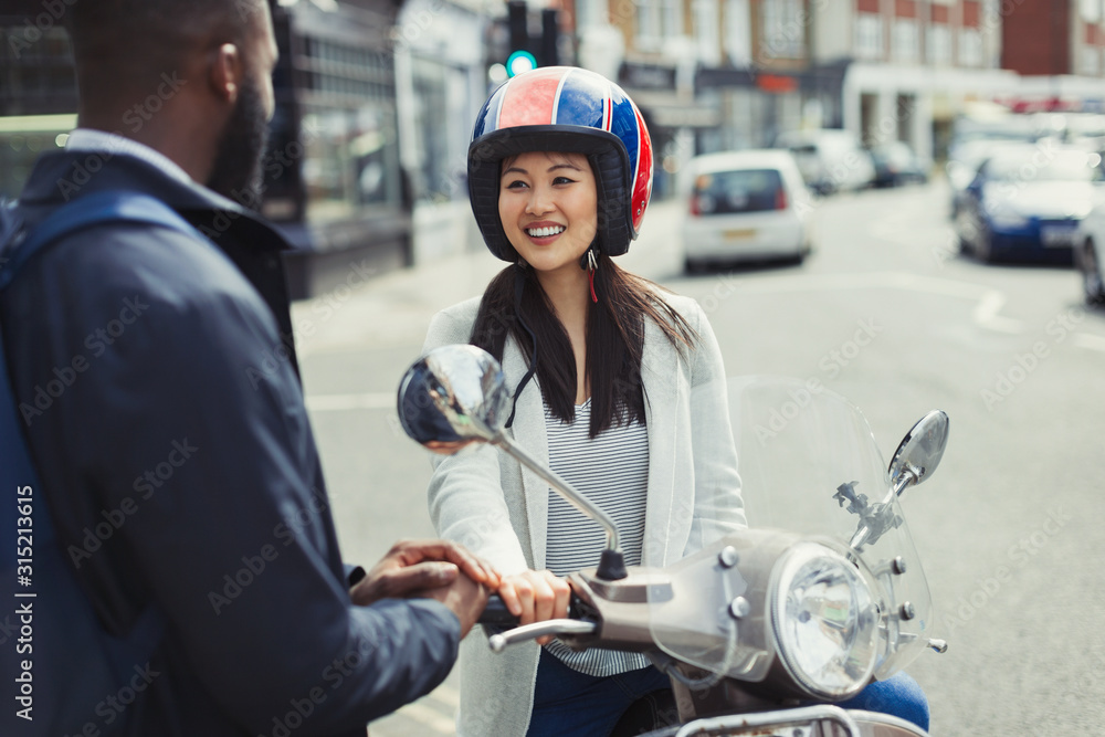 Smiling young woman on motor scooter talking to friend on sunny urban street Smiling young woman on motor scooter talking to friend on sunny urban street