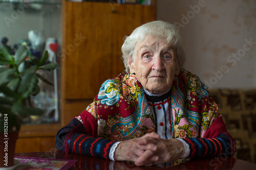 An elderly woman in Slavic clothes sitting in home.