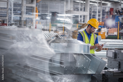 Factory worker with clipboard inspecting steel parts in factory