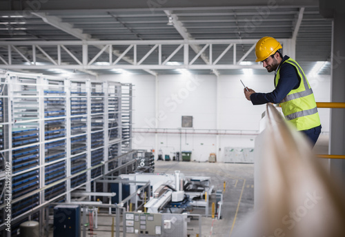 Male supervisor with clipboard on platform looking down at factory