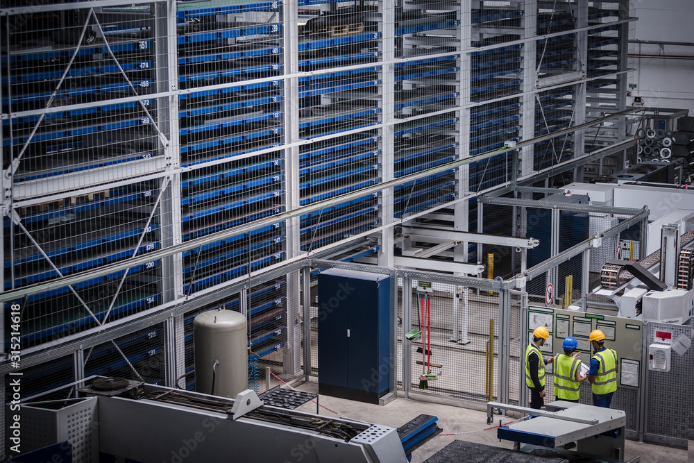 Supervisor and workers discussing information hanging on wall in factory