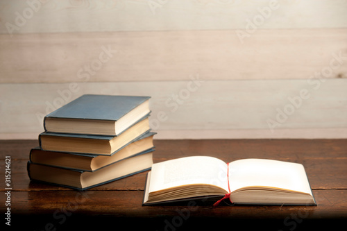 stack of books on wooden desk, with open book