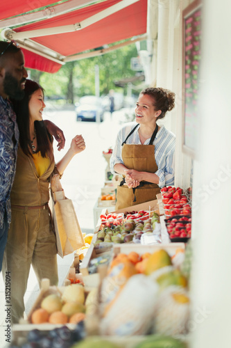 Female worker helping young couple shopping for fruit at market storefront photo