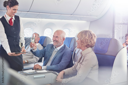 Flight attendant serving champagne to mature couple in first class on airplane
