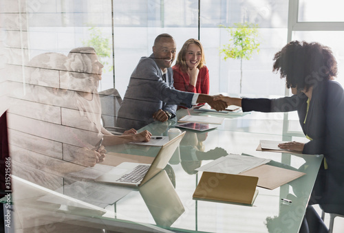 Businessman businesswoman handshaking across conference table in meeting