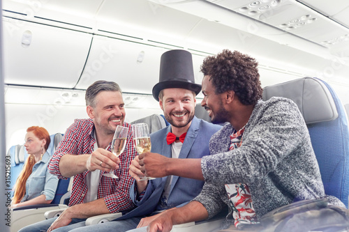 Young male friends toasting champagne glasses in first class on airplane
