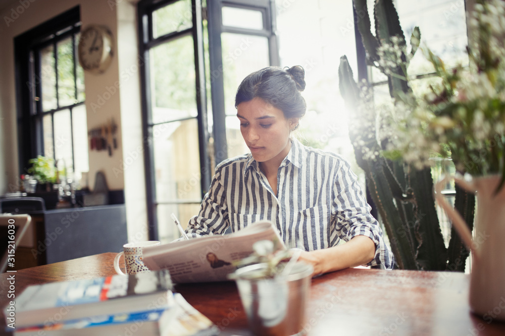 Young woman with newspaper at dining room Young woman with newspaper at dining room