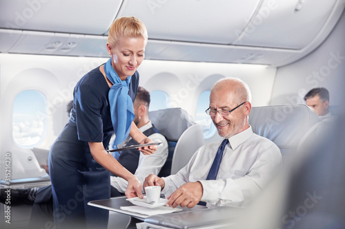 flight attendant serving espresso coffee to businessman in first class on airplane photo