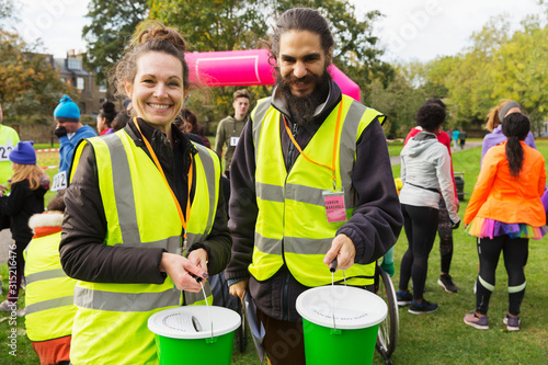 Portrait smiling volunteers donation buckets at charity run in park photo