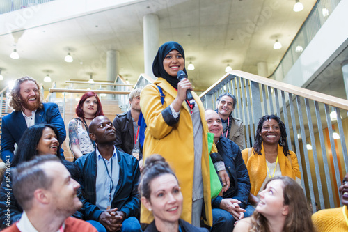 Smiling woman in hijab speaking with microphone in conference audience