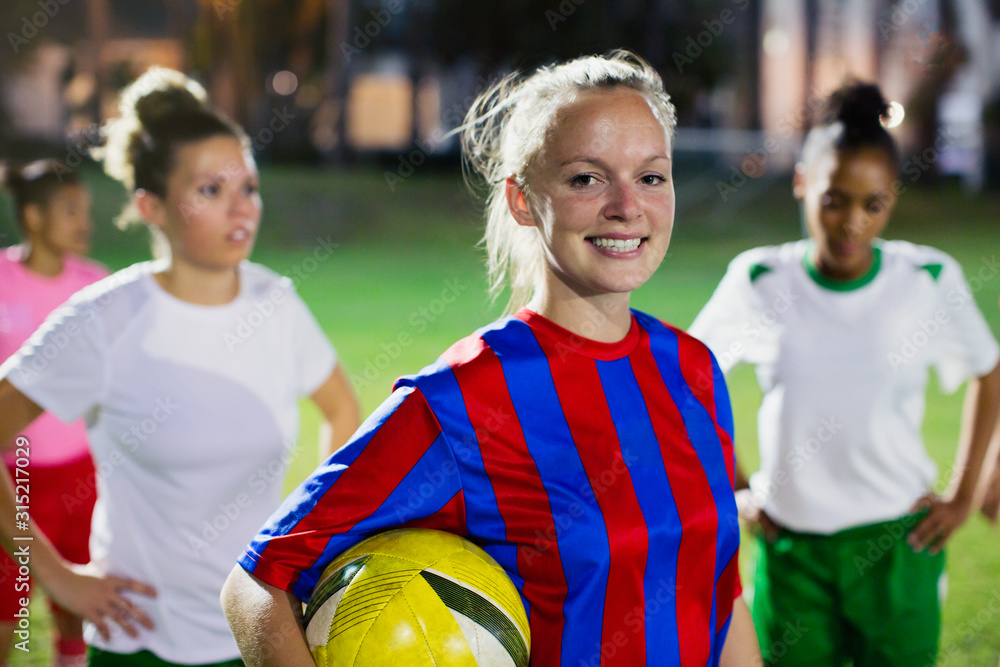 Portrait smiling, confident young female soccer player ball on field at night Portrait smiling, confident young female soccer player ball on field at night
