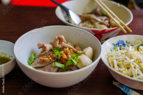 Close up view of Spicy Thai Boat rice Noodle Soup, Kuai Tiao Ruea, serve on ceramic bowl on wooden table with fresh bean sprouts on side. 