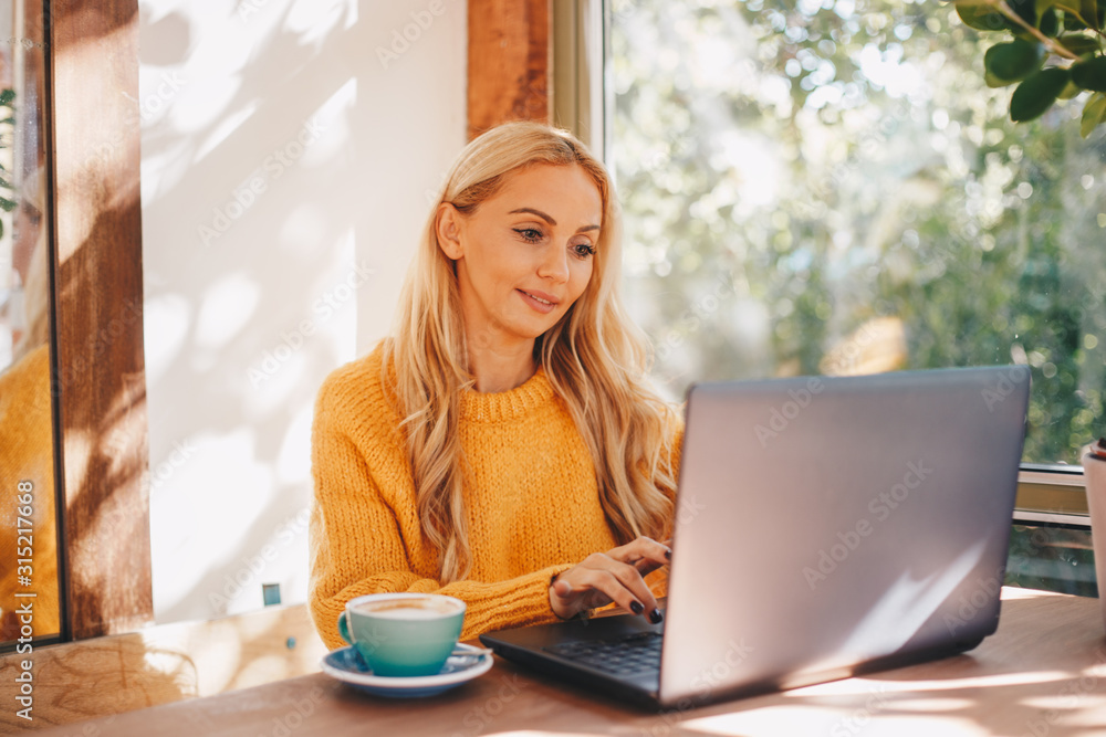 A woman using a laptop drinking coffee indoors. A woman using a laptop drinking coffee indoors.