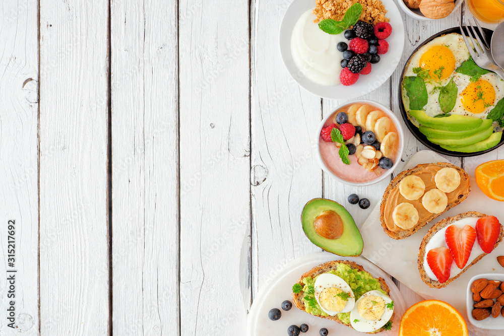 Healthy breakfast food side border. Table scene with fruit, yogurt, smoothie, nutritious toasts and egg skillet. Above view over a white wood background. Copy space.