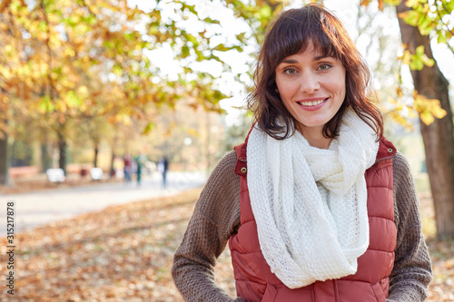 Portrait smiling woman in vest and scarf in sunny autumn park