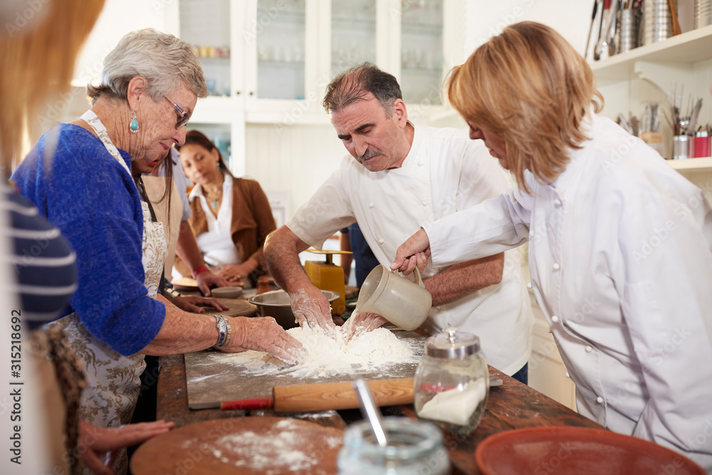 Chef and senior woman making pizza dough flour nest in cooking class