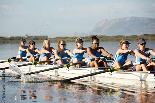 Female rowers rowing scull on sunny lake