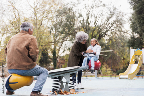 Grandparents playing with granddaughter on seesaw at playground photo