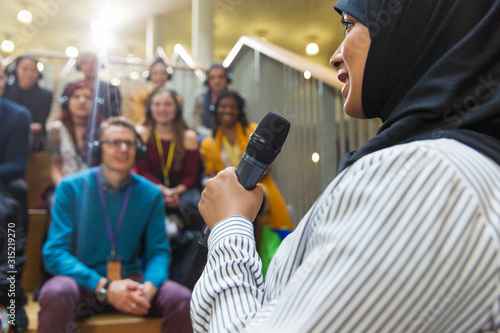 Smiling businesswoman in hijab speaking to audience with microphone photo