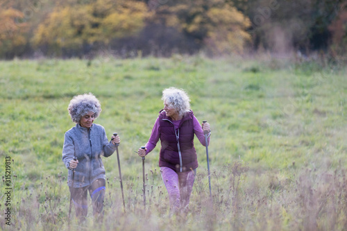 Active senior women friends hiking with poles up rural hillside