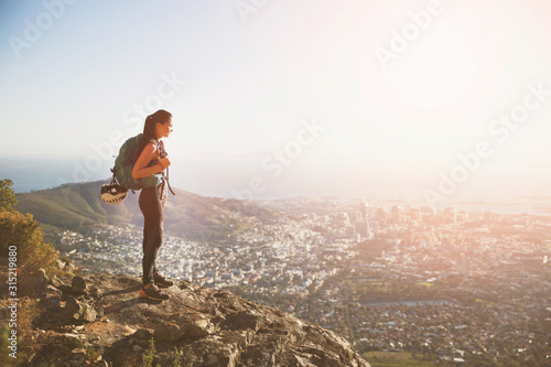 Female rock climber on top of hill overlooking sunny city photo